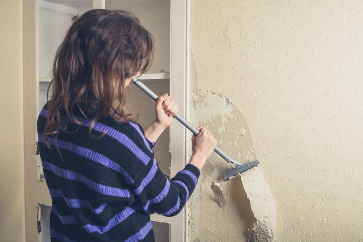 woman scrapes wallpaper off wall