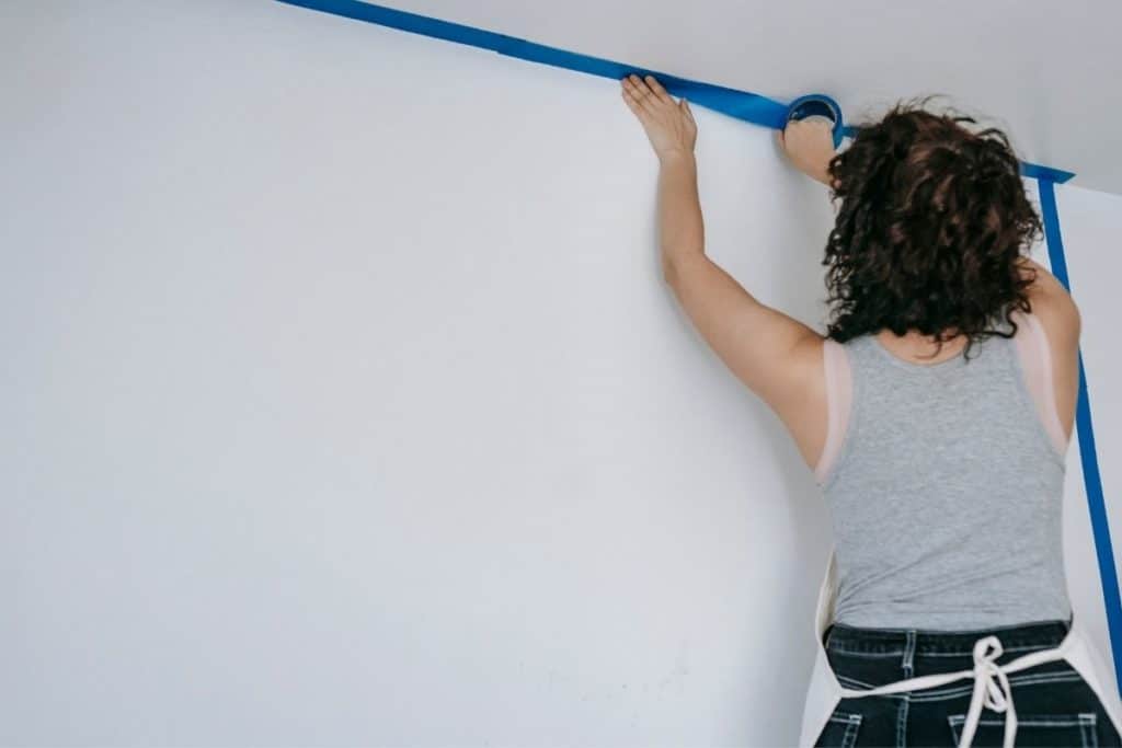 woman applies painters tape to ceiling